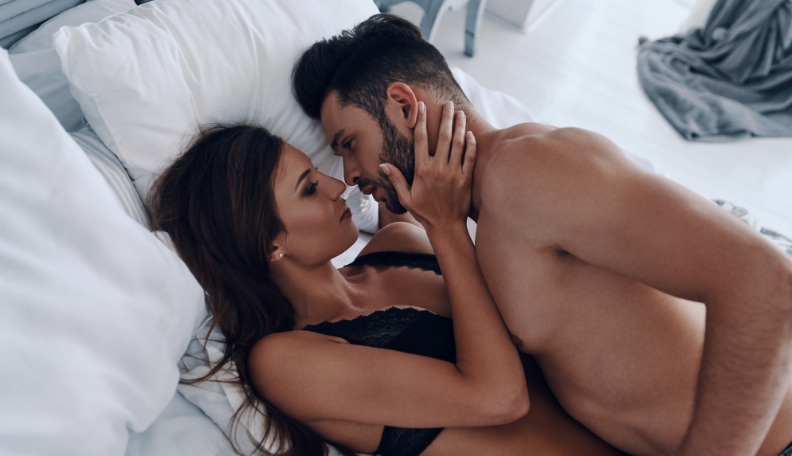 Man with beards having sex with a black haired woman on a white bed 