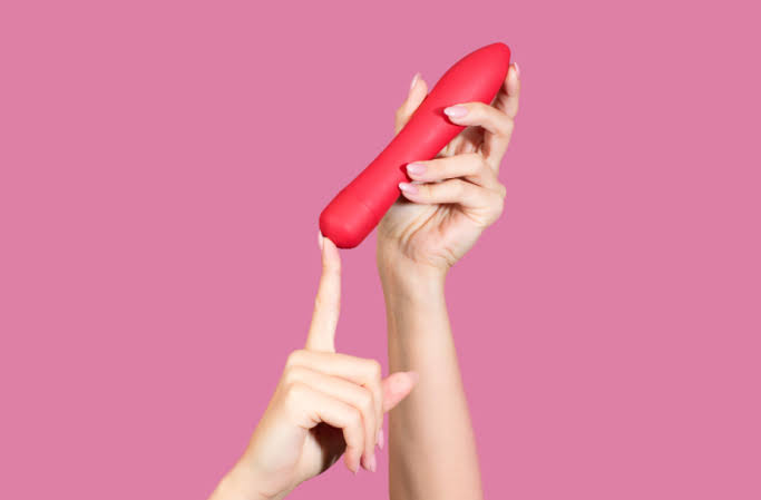 Hand holding up a red sex toy used for making a girl orgasm